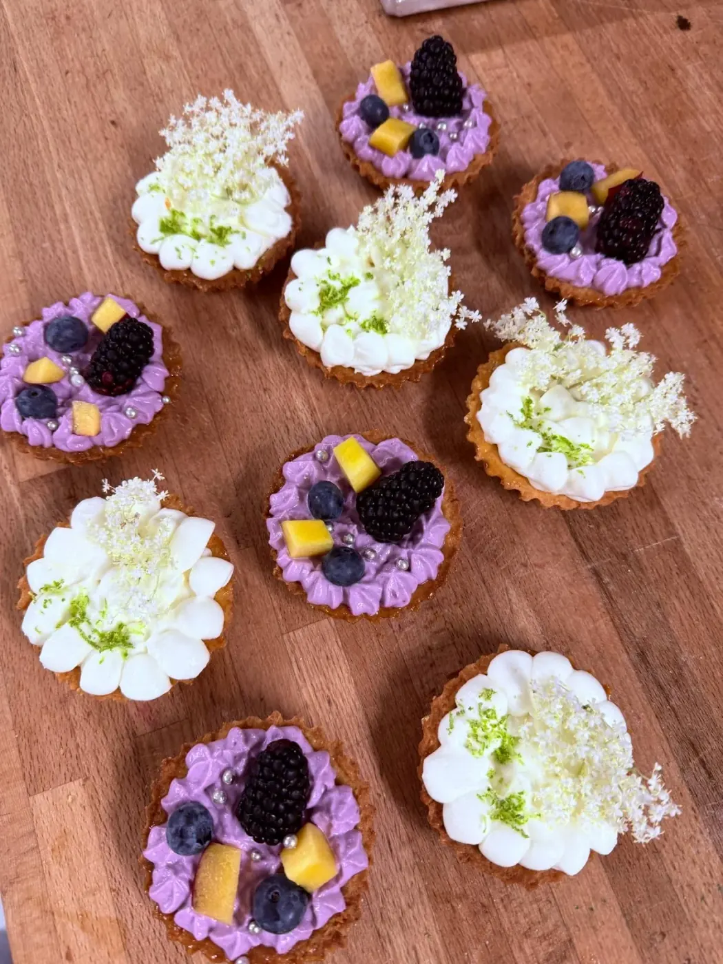 Pasticcini con fiori di sambuco, crema ai frutti di bosco e more su un tavolo di legno