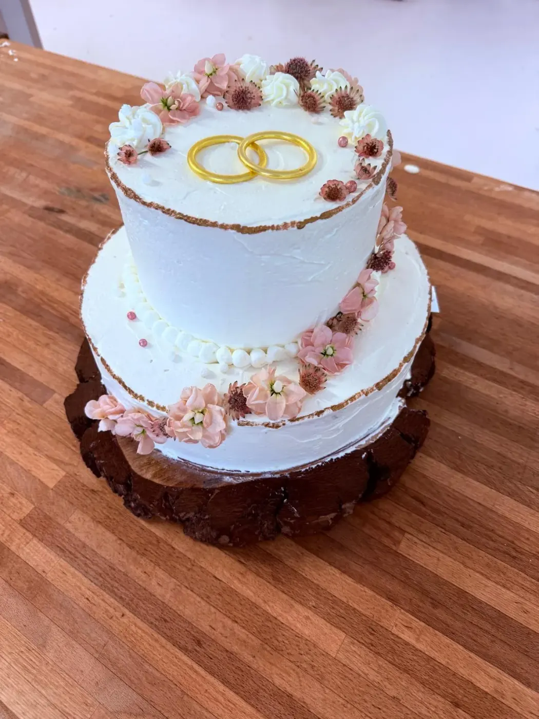 Torta nuziale bianca a due piani con anelli dorati e fiori rosa